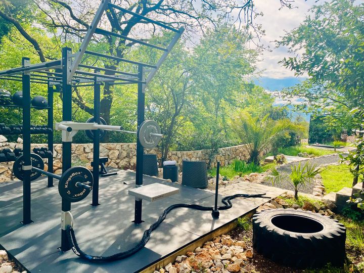open-air fitness deck with weights and battle rope, the sea beyond the trees
